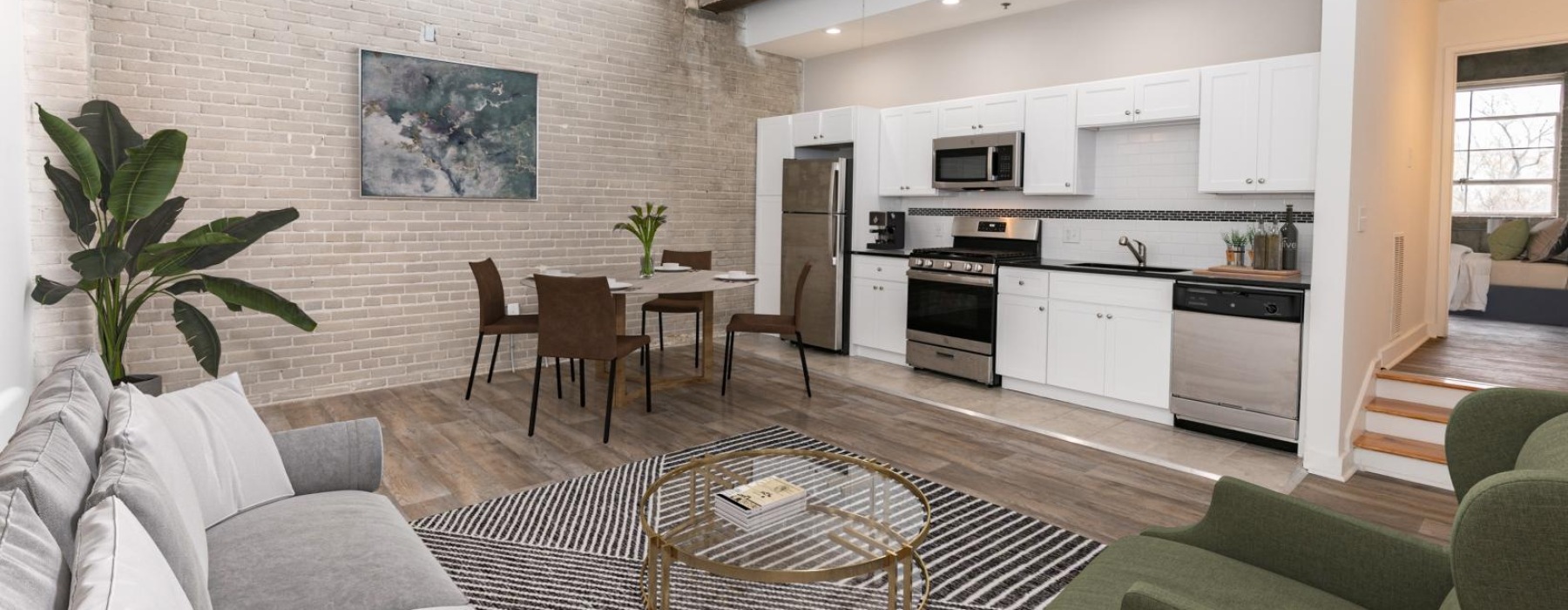 Modern open-concept loft with a white kitchen, dining area, and living space featuring contemporary furniture and large windows—perfect for those seeking stylish apartments for rent in Atlanta, GA.